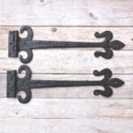 Hand forged wrought iron Fleur de Lis strap hinges with rustic black finish. Heavy-duty decorative hinges for barn doors, gates, sheds, garages, farmhouse, and restoration projects.