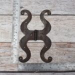 Pair of decorative black cast iron butterfly scroll hinges on a light wooden background.