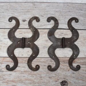 Pair of decorative black cast iron butterfly scroll hinges on a light wooden background.