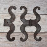 Pair of decorative black cast iron butterfly scroll hinges on a light wooden background.