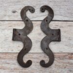 Pair of decorative black cast iron butterfly scroll hinges on a light wooden background.