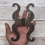 Pair of decorative black cast iron butterfly scroll hinges on a light wooden background.