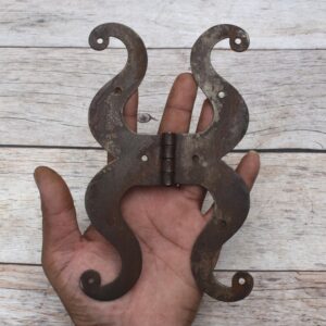 Pair of decorative black cast iron butterfly scroll hinges on a light wooden background.