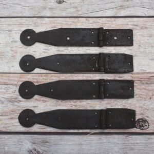 Set of four dark iron penny-end strap hinges on a light wood plank surface.