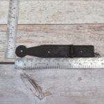 Set of four dark iron penny-end strap hinges on a light wood plank surface.