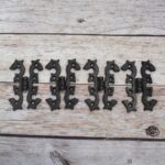 Pair of decorative black cast iron butterfly scroll hinges on a light wooden background.