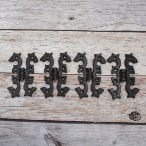 Pair of decorative black cast iron butterfly scroll hinges on a light wooden background.