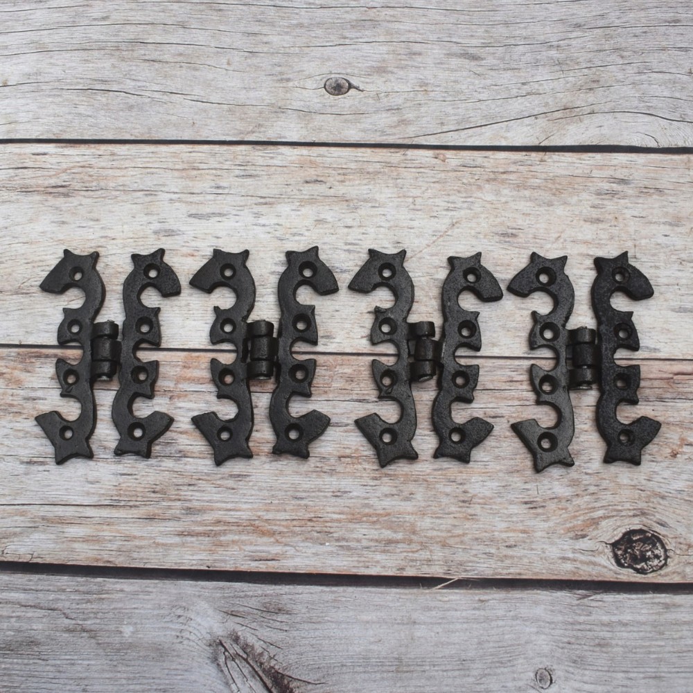 Pair of decorative black cast iron butterfly scroll hinges on a light wooden background. Pair of decorative black cast iron butterfly scroll hinges on a light wooden background.
