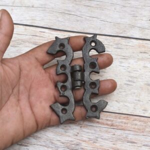 Pair of decorative black cast iron butterfly scroll hinges on a light wooden background.