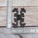 Pair of decorative black cast iron butterfly scroll hinges on a light wooden background.